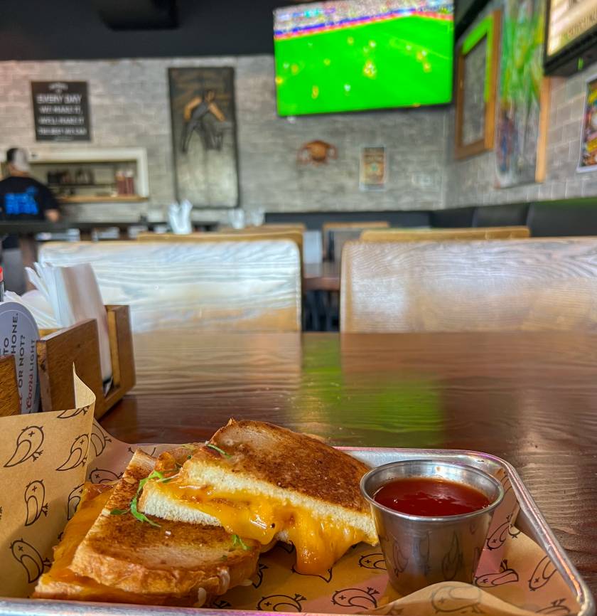 grilled cheese on table and soccer game on tv