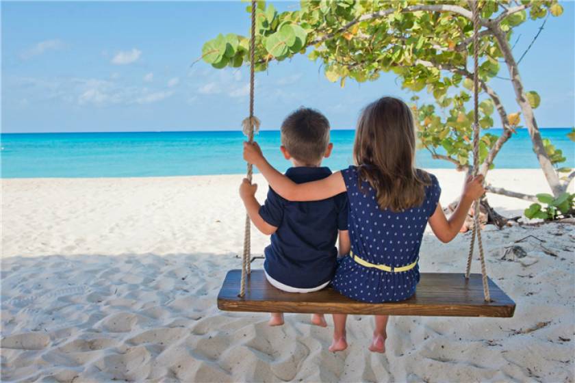 two kids sitting on swing on beach