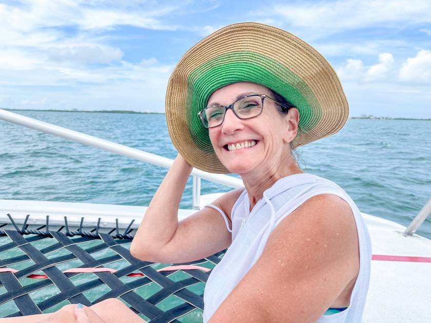 karen at front of boat beach hat blowing back